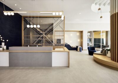 Modern hotel lobby with minimalist décor, light wood and white finishes, a geometric wall art piece, and contemporary seating areas.