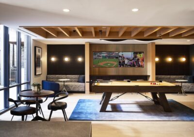 A modern game room with a pool table, round dining table with four chairs, two sofas, and a TV displaying a baseball game on the back wall.
