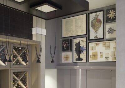 A wall displays framed art, including vintage documents, a hot air balloon illustration, a silhouette portrait, and abstract pieces, above a modern wine rack and cabinets.