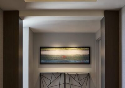 A hallway with a large ceiling light, tiled floor, abstract wall art, and a decorative metal console table beneath the painting.