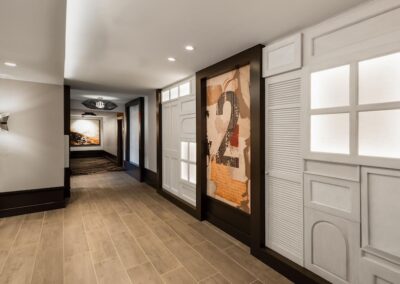 A modern hotel hallway with wood flooring, white paneled walls, wall art featuring the number 2, and recessed lighting.