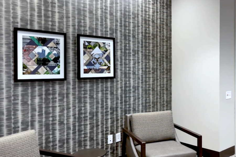 A modern waiting area with a gray armchair, small round table, patterned wallpaper, and two framed abstract artworks on the wall.