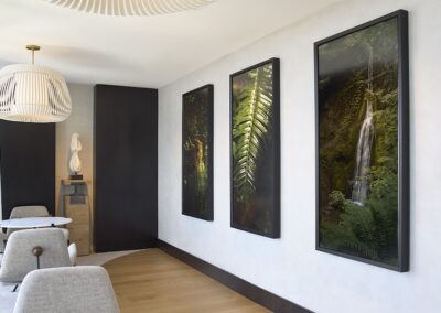 A modern sitting area with two grey chairs, a light wood floor, and three large nature-themed framed artworks on a white wall.