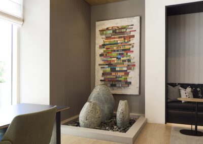 A modern interior features a corner with large decorative rocks on pebbles and a colorful abstract artwork on the wall above them.