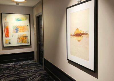 A hallway with two framed abstract art pieces on beige walls, a dark door, patterned carpet, and a ceiling light.