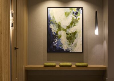 A modern entryway with a wooden bench, three round green cushions, abstract wall art, and a hanging pendant light.