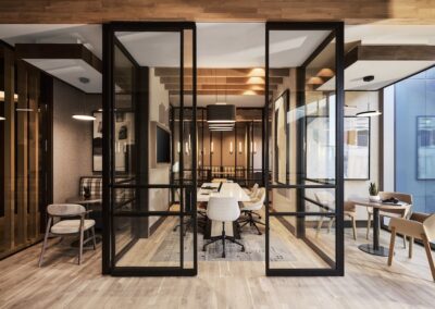 Modern conference room with glass walls, wooden floors, a large table with chairs, and an adjoining office area with desks and seating.