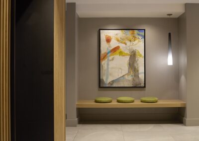 A minimalist hallway with three round green cushions on a bench, a large abstract painting on the wall, and a single hanging light fixture.
