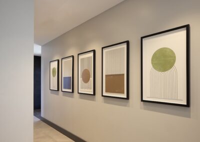 A hallway with beige walls displays five framed abstract art prints in a row, each featuring geometric shapes and minimalistic designs in muted colors.