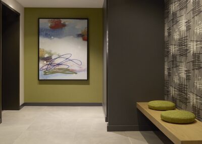 Modern hallway with abstract wall art, a wooden bench with two round green cushions, and patterned wallpaper on the right wall.