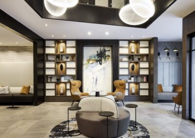 Modern hotel lobby with abstract artwork, contemporary seating, decorative shelves, and round hanging lights, featuring neutral tones and stylish decor.
