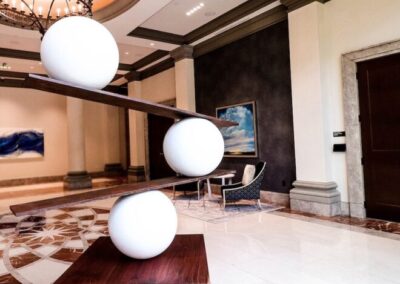 A sculpture of three large white spheres stacked diagonally on a wooden base in a modern, elegant lobby with marble floors and contemporary decor.