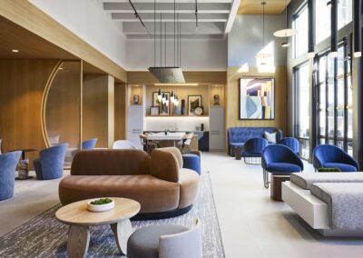 Modern lounge with brown and blue seating, a wooden coffee table, large windows, wall art, and pendant lighting in a bright, open space.