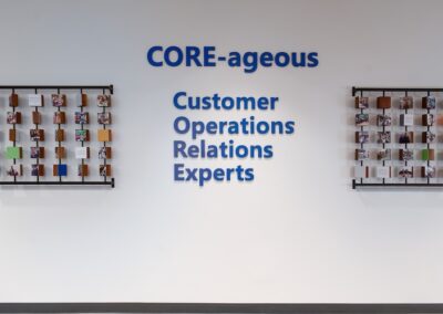 A wall display with the text "CORE-ageous Customer Operations Relations Experts" flanked by two grids holding cards and photos.