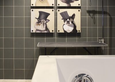 A modern bathroom with a white bathtub, wall-mounted shower, and four framed animal portraits in top hats on a tiled wall.