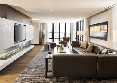 Modern living room with a sectional leather sofa, flat-screen TV, fireplace, large windows, contemporary decor, and neutral color tones.