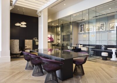 Modern office space with a long black table, purple chairs, glass-walled meeting rooms, wood flooring, and contemporary decor.