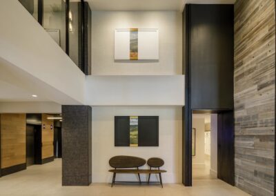Modern lobby area with a wooden bench, two framed artworks on the wall, and light-colored tile flooring. Dark and wood accents decorate the space.
