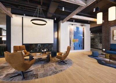Modern lounge with four brown chairs around a circular coffee table, abstract art on the wall, and exposed ceiling beams and brick accents.