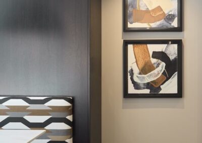 Two abstract paintings in black frames hang on a beige wall next to a built-in bench with geometric-patterned upholstery.