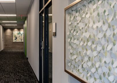 A modern office hallway with patterned carpet, white walls, and two large abstract artworks hanging on the walls.