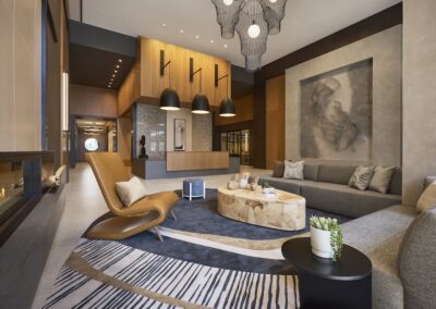 Modern lobby with contemporary furniture, large abstract wall art, pendant lights, and natural wood accents. A fireplace is visible on the left, and a reception desk in the background.