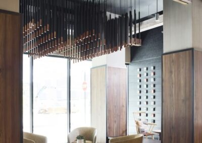 Modern lounge area with four beige armchairs around a small coffee table, geometric floor tiles, wood paneling, and a decorative hanging ceiling installation.