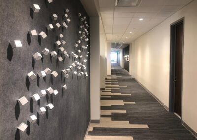A modern hallway with geometric wall art featuring small silver cubes on a dark wall and patterned carpet tiles along the corridor.