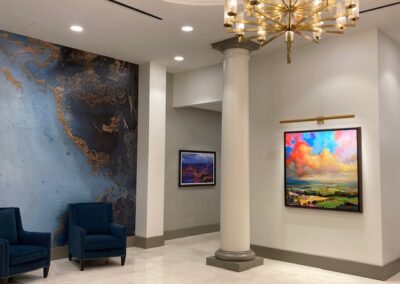 Lobby interior with blue chairs, a large map of North America on one wall, two colorful landscape paintings, a column, and a modern chandelier.