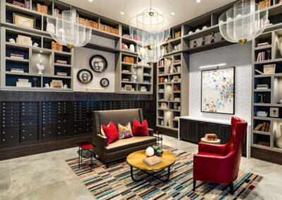 Modern library room with wall-to-wall shelving, red armchairs, a gray sofa, decorative objects, and contemporary art under large mesh ceiling lights.