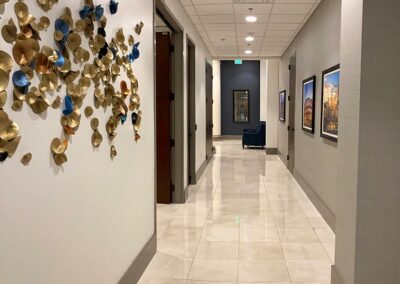 A clean, well-lit hallway with tiled floors, framed pictures on the right wall, and gold and blue decorative art on the left wall.