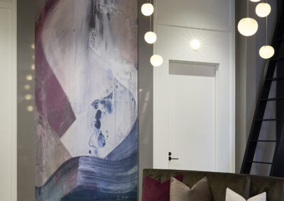 A modern living room with a large abstract painting on the wall, a curved sofa with pillows, a round table, and hanging globe pendant lights.