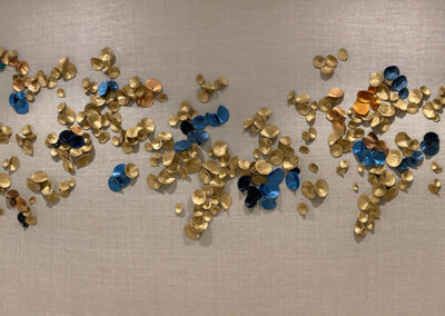 Wall-mounted abstract art featuring clusters of circular gold, blue, and copper metallic discs arranged against a neutral background.