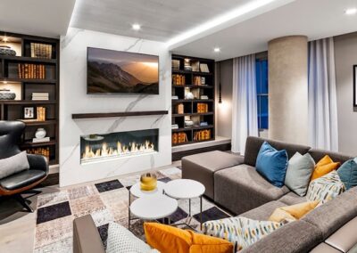 Modern living room with a sectional sofa, pillows, built-in bookshelves, a fireplace under a wall-mounted TV, and contemporary decor.