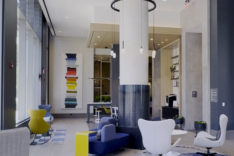 Modern lobby with contemporary chairs, round tables, a central column, large windows, abstract wall art, and neutral tones with colorful accents.