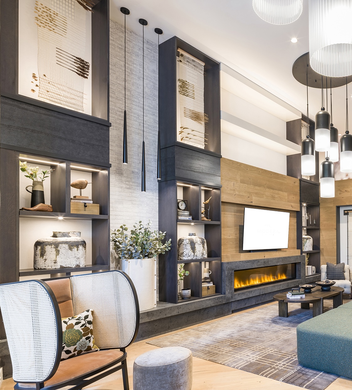 Modern living room with built-in shelving, contemporary decor, large wall-mounted TV, electric fireplace, pendant lights, and neutral-toned furniture.